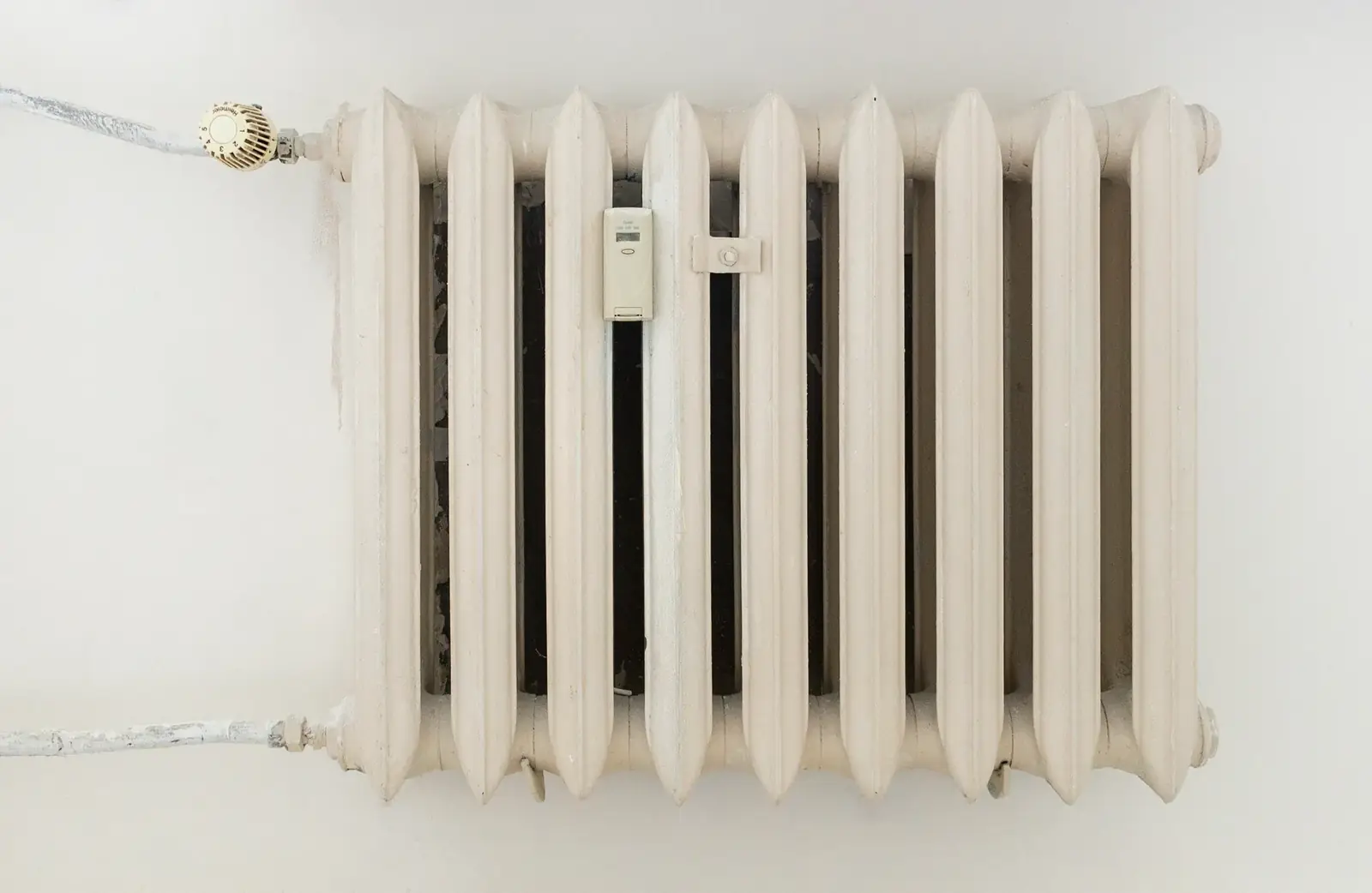 A classic white metal radiator on a plain wall, showcasing minimalist interior design.