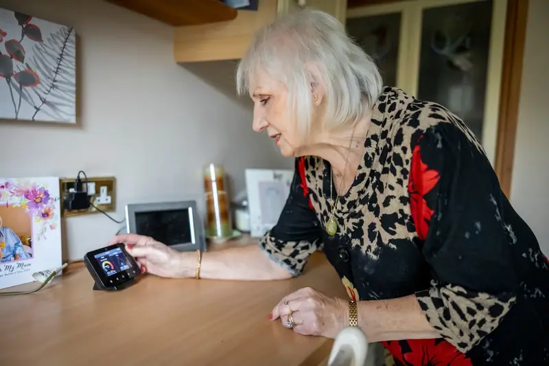 An elderly woman interacts with a smart meter on a desk, illustrating energy management in modern technology.
