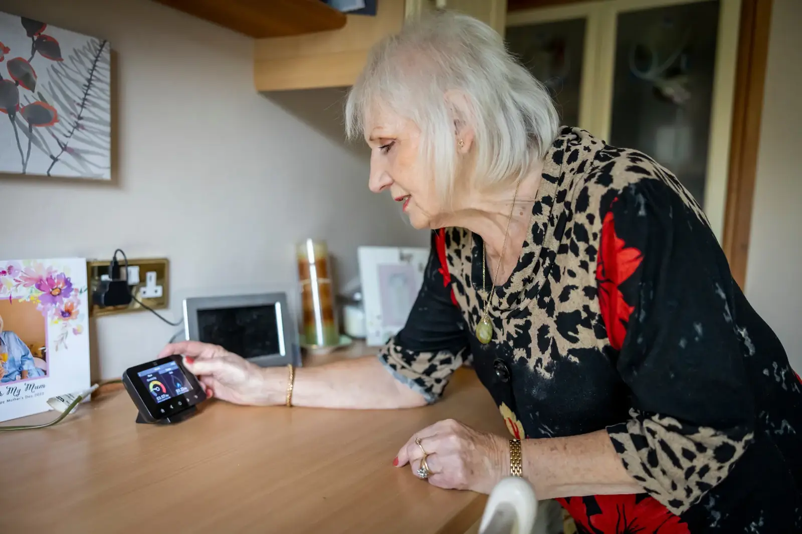 An elderly woman interacts with a smart meter on a desk, illustrating energy management in modern technology.