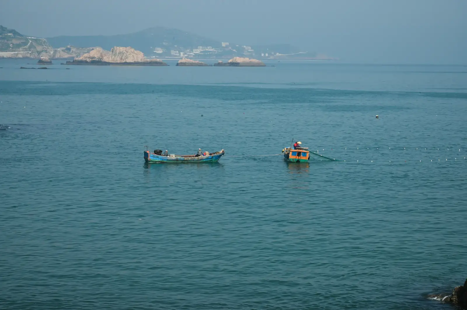 Fishing boats with nets cast on a tranquil blue sea with a distant coastal view.