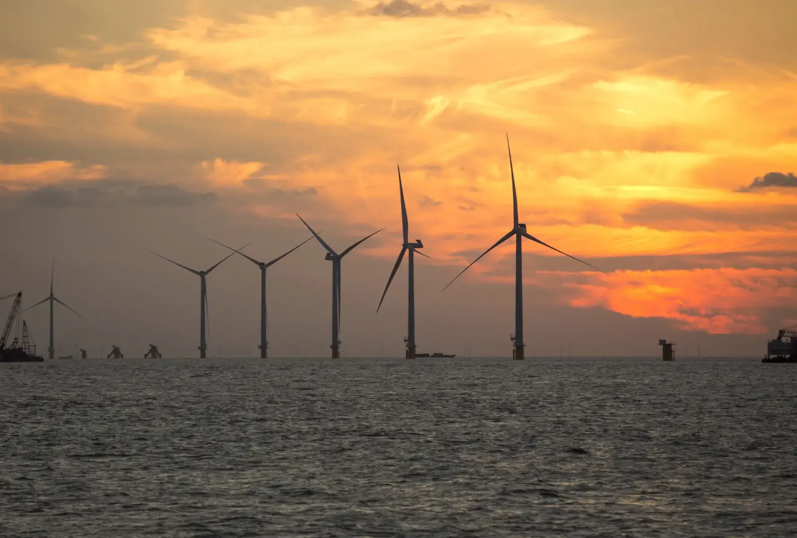 A serene view of wind turbines silhouetted against a vibrant sunset over the sea, showcasing renewable energy.