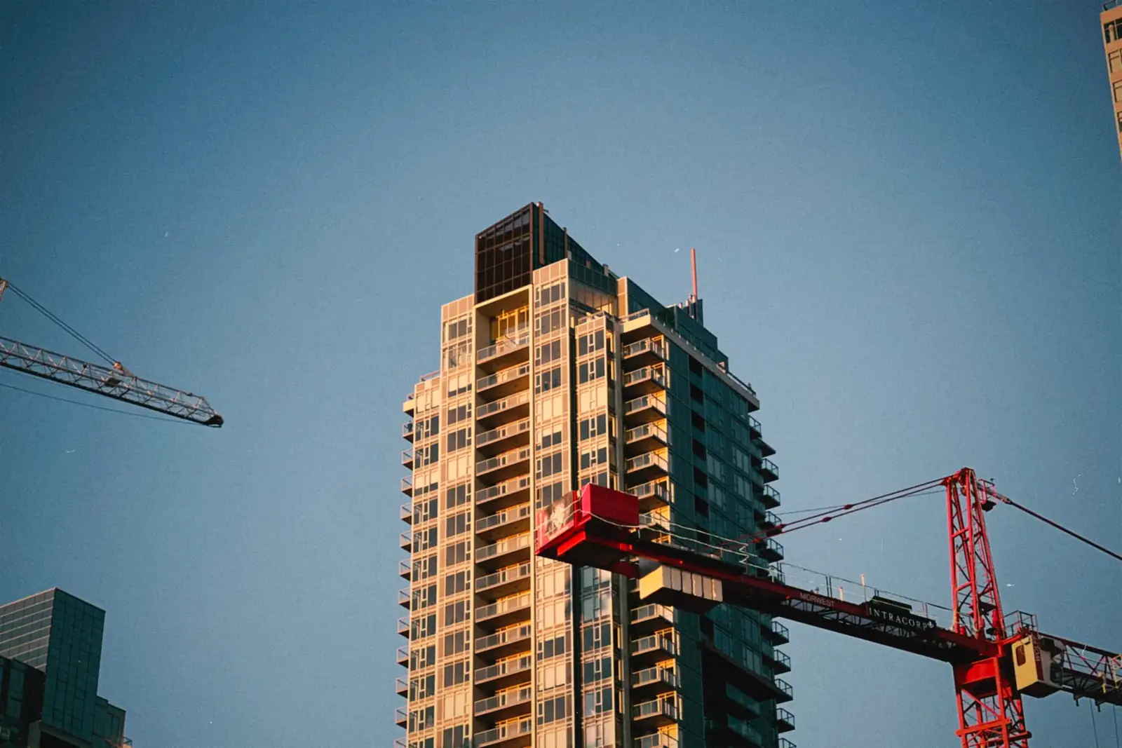 High-rise building with cranes in urban area against blue sky backdrop.