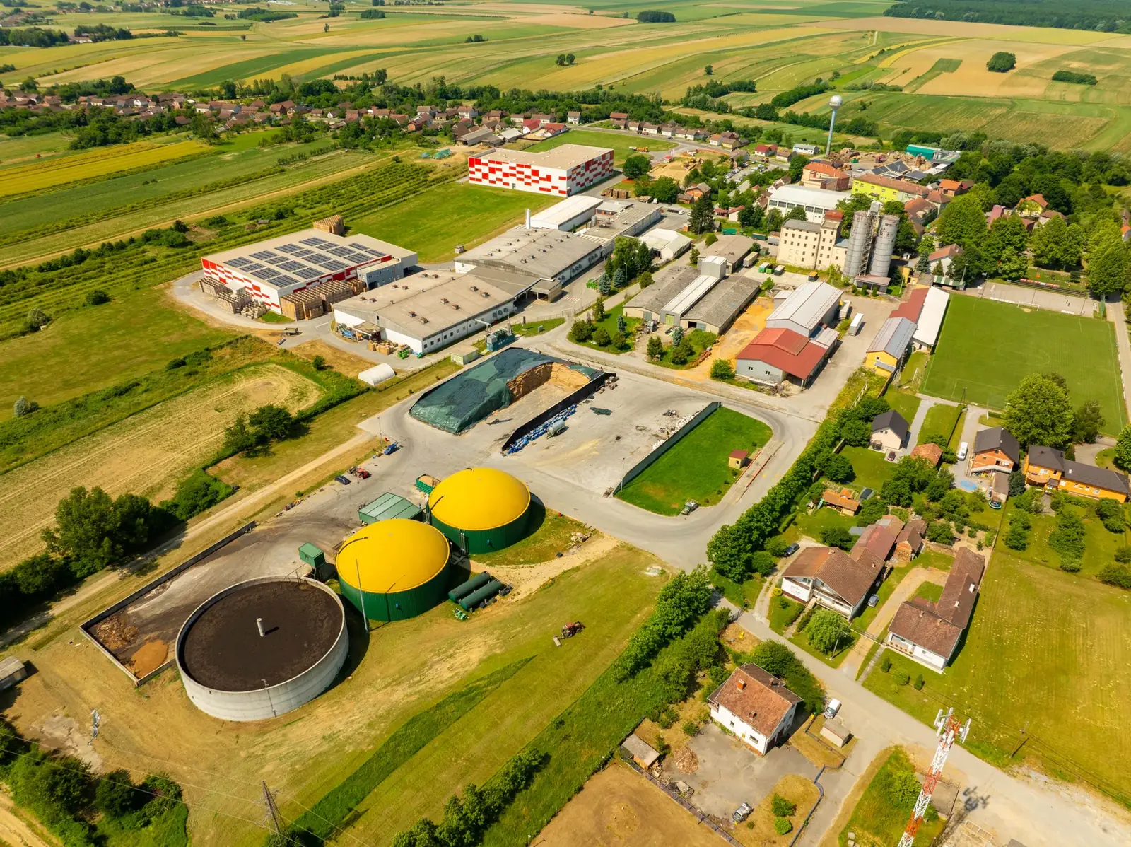 Aerial view of a biogas plant with anaerobic digester tanks beside farmland.