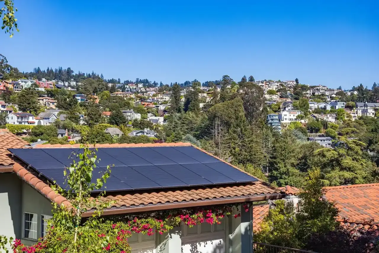 Solar panels on a suburban home, surrounded by lush greenery and a sunny blue sky.