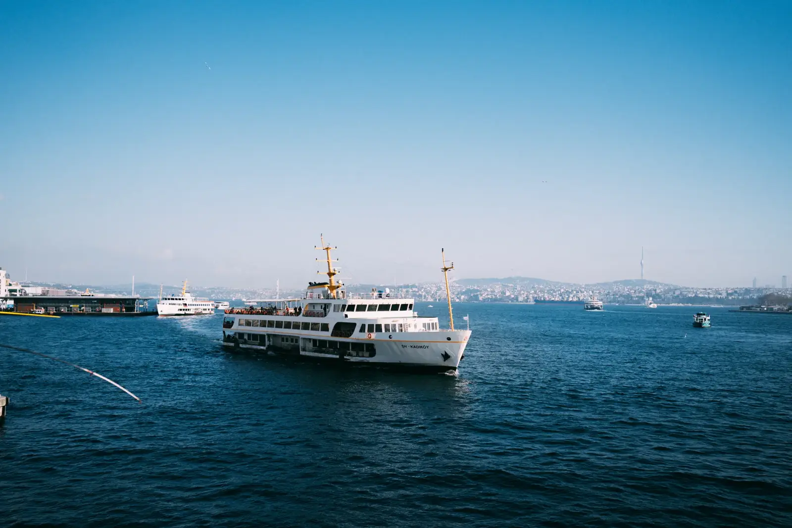 A ferry sails on the Bosphorus in Istanbul with a cityscape background under a clear blue sky.