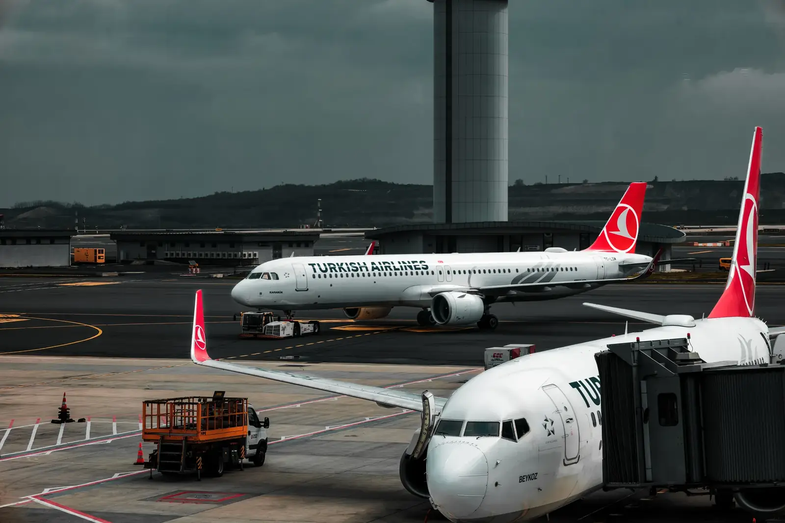Turkish Airlines planes parked at an airport with a control tower in the background.