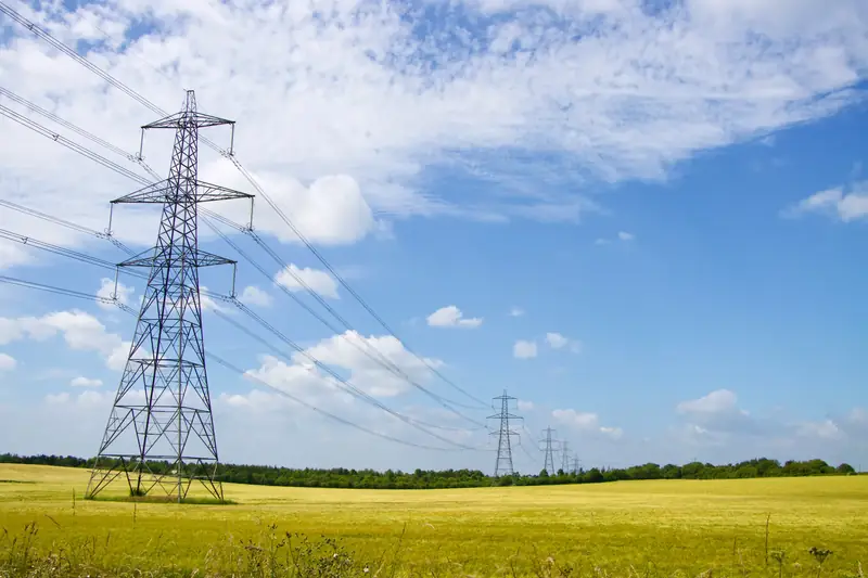 Power pylons in a green field under a bright blue sky in England.