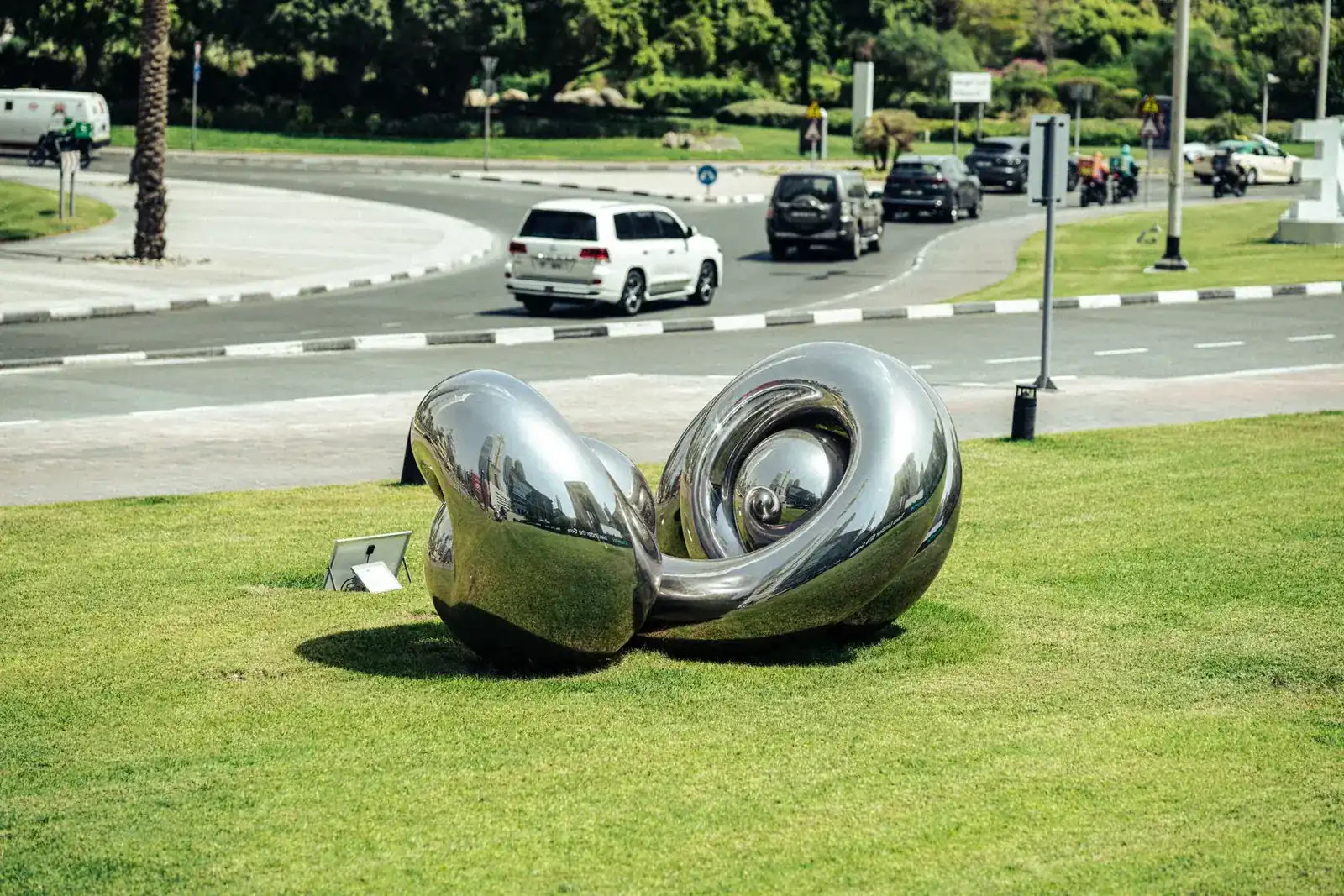 Stainless steel sculpture on a lawn in urban Dubai, reflecting modern art aesthetics.