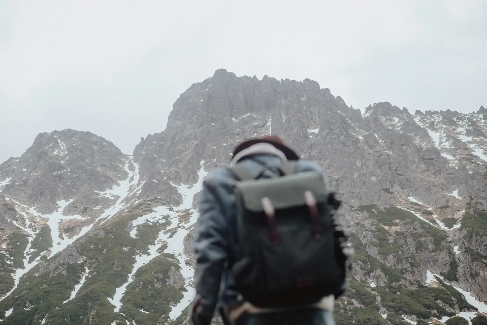 Traveler with backpack gazing at rugged, snowy mountain landscape.
