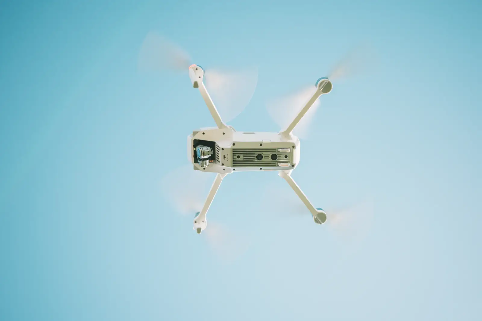 A sleek white drone flying under a clear blue sky, capturing aerial views.