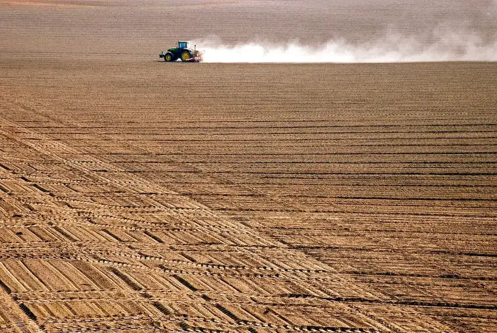 A tractor plowing through a vast, freshly tilled agricultural field during the day.