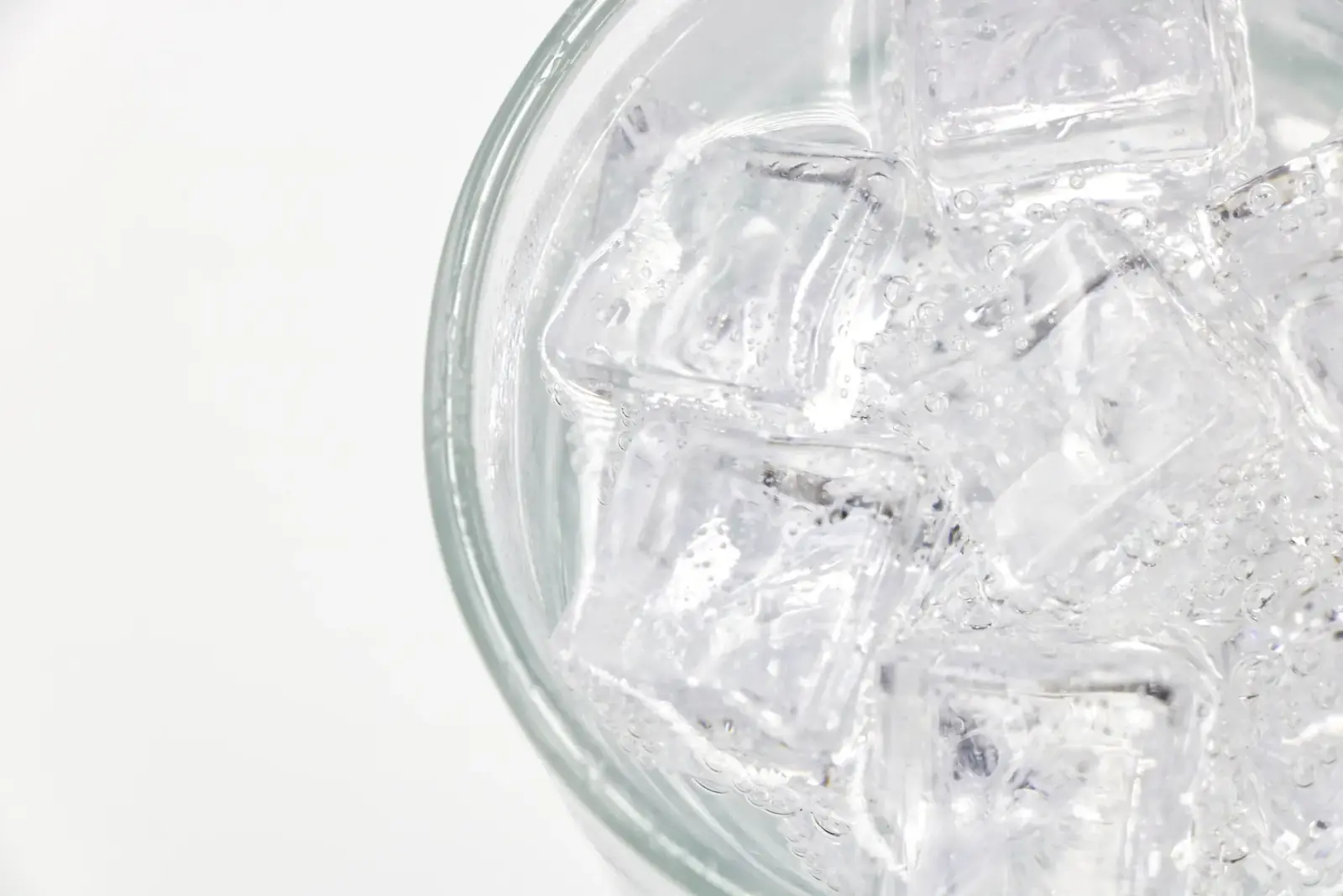 Close-up of a glass filled with sparkling water and ice cubes on a white background.