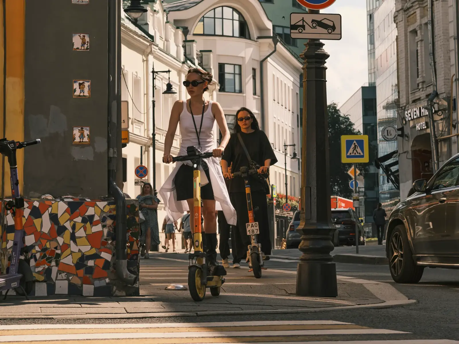 Two women riding electric scooters on a city street, showcasing urban commute.