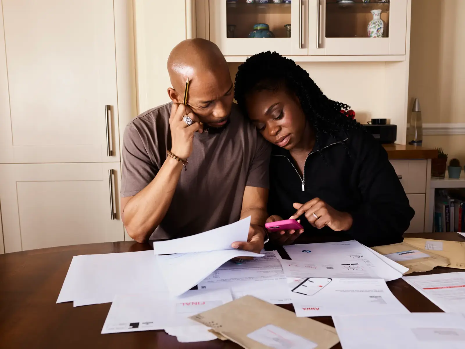 A couple sits at a table managing domestic finances, evaluating documents and using a smartphone.