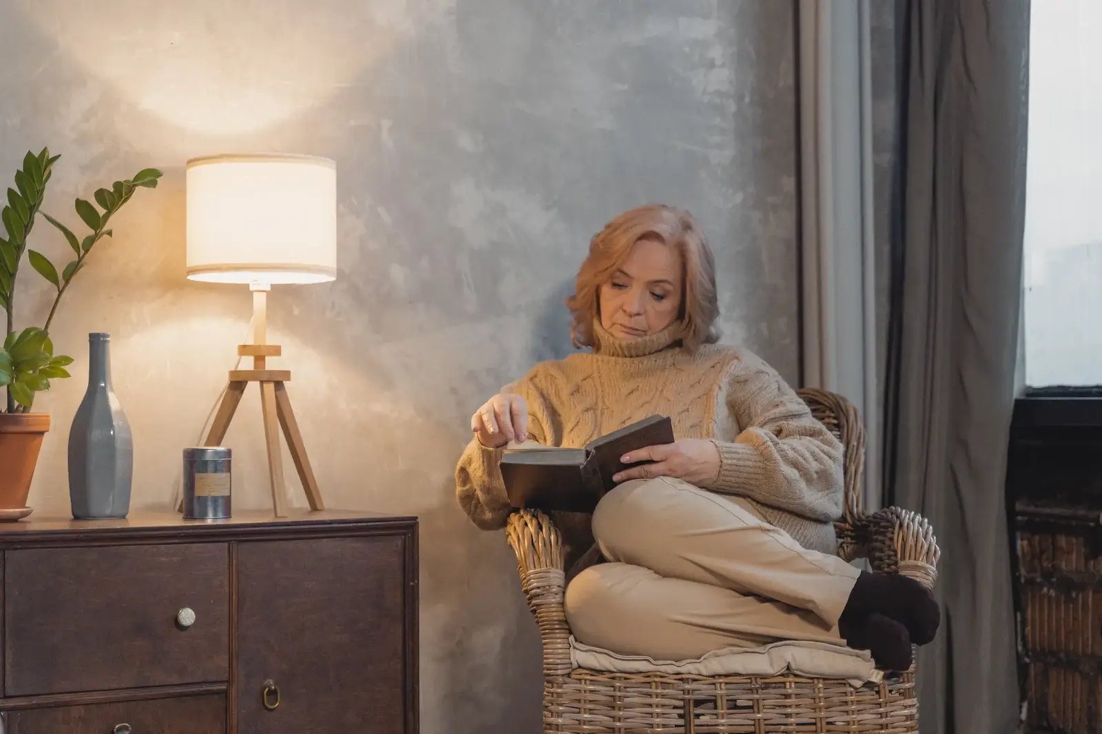 Elderly woman enjoying a tranquil moment reading on a comfortable chair indoors.